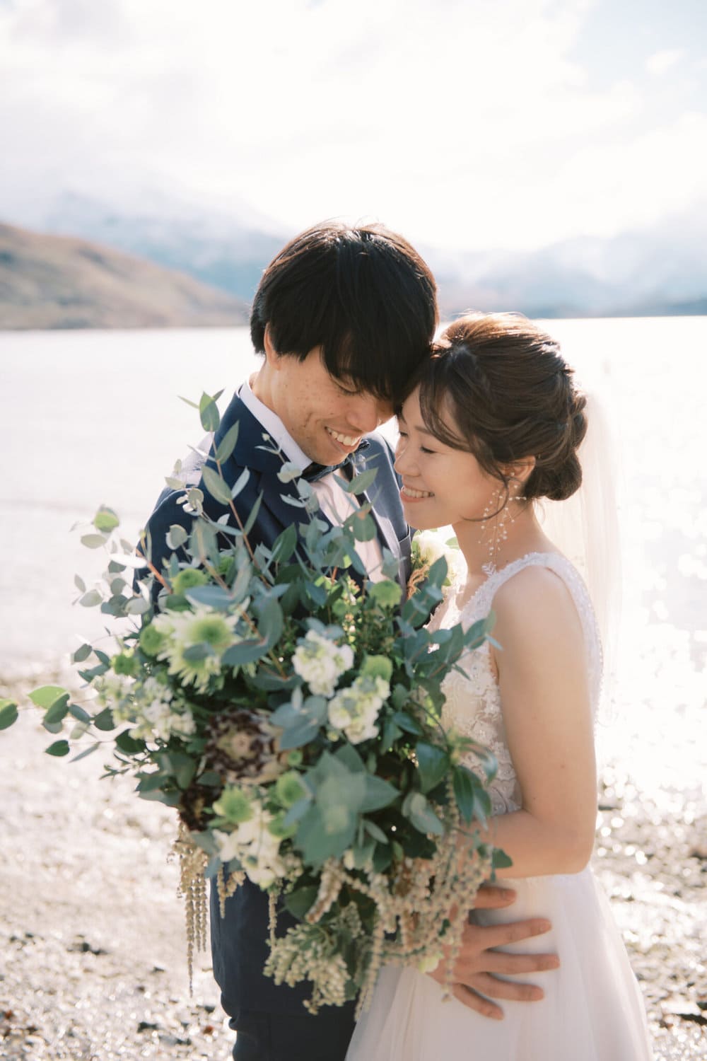 Queenstown Tekapo New Zealand Heli Wedding Elopement Pre-Wedding Shoot Photographer クイーンズタウン　テカポ　ニュージーランド　エロープメント 前撮り　フォトウェディング　結婚式 | A couple in wedding attire sharing an intimate moment by Lake Tekapo with mountains in the background during their pre-wedding shoot.